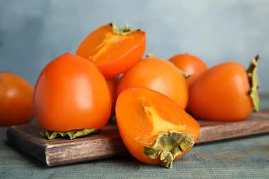 Photo of Tasty ripe persimmons on light blue wooden table, closeup