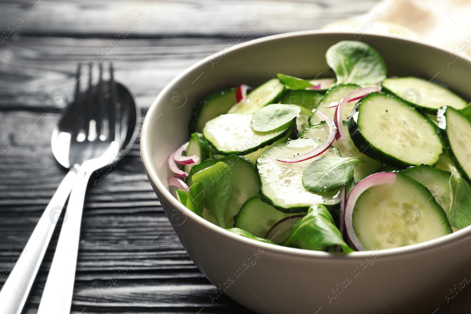 Photo of Delicious cucumber salad with onion and spinach in bowl on wooden table, closeup