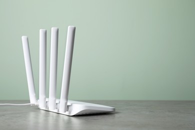 Photo of New modern Wi-Fi router on grey table near green wall, space for text