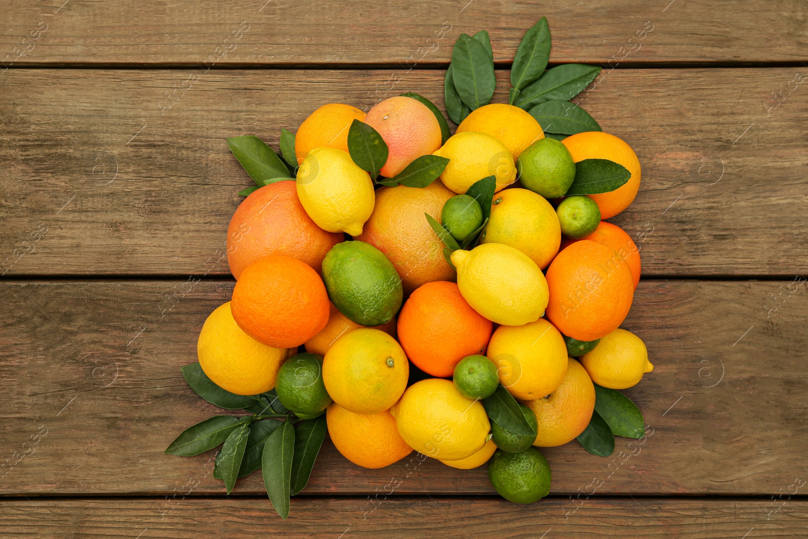 Photo of Different citrus fruits with green leaves on wooden table, flat lay