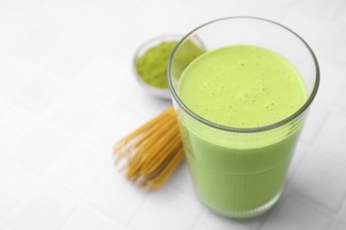 Photo of Glass of tasty matcha smoothie, powder and bamboo whisk on white tiled table, closeup. Space for text