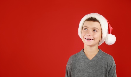 Happy little child in Santa hat on red background, space for text. Christmas celebration