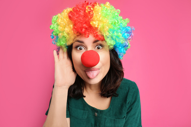 Photo of Funny woman with rainbow wig and clown nose on pink background. April fool's day