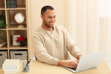 Photo of Smiling African American man typing on laptop at wooden table in room