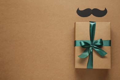 Gift box and paper mustache on brown background, flat lay with space for text. Father's day celebration