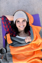 Female camper lying in sleeping bag on sand, top view
