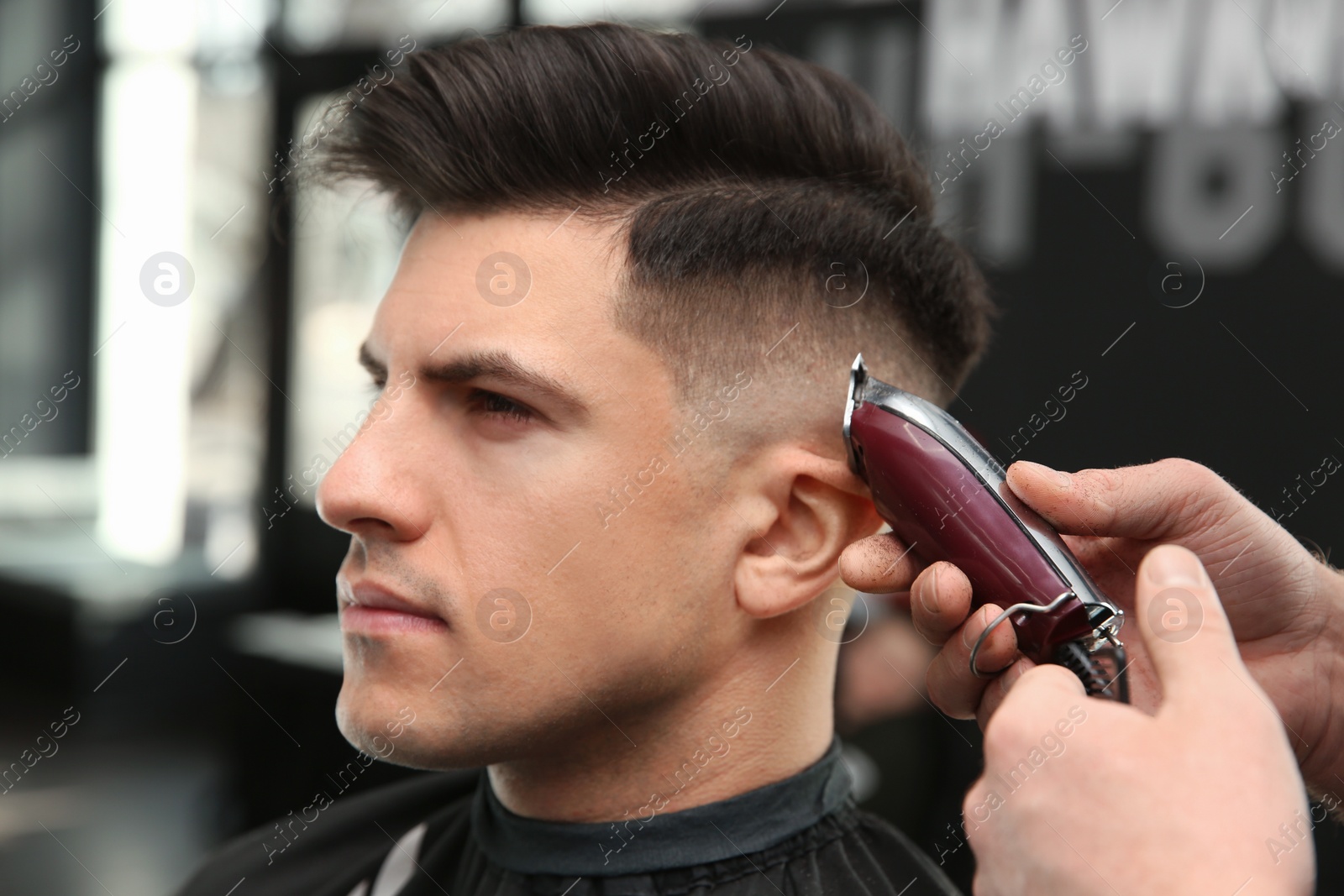 Photo of Professional barber making stylish haircut in salon, closeup