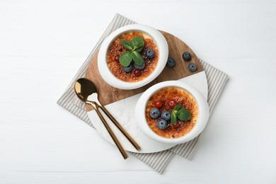 Photo of Delicious creme brulee with berries and mint in bowls on white wooden table, top view