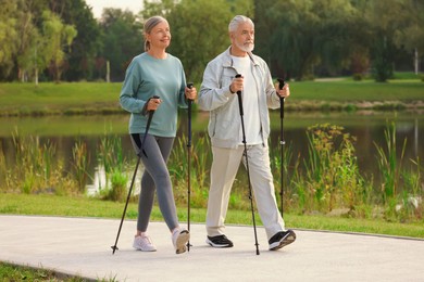 Photo of Senior man and woman performing Nordic walking outdoors