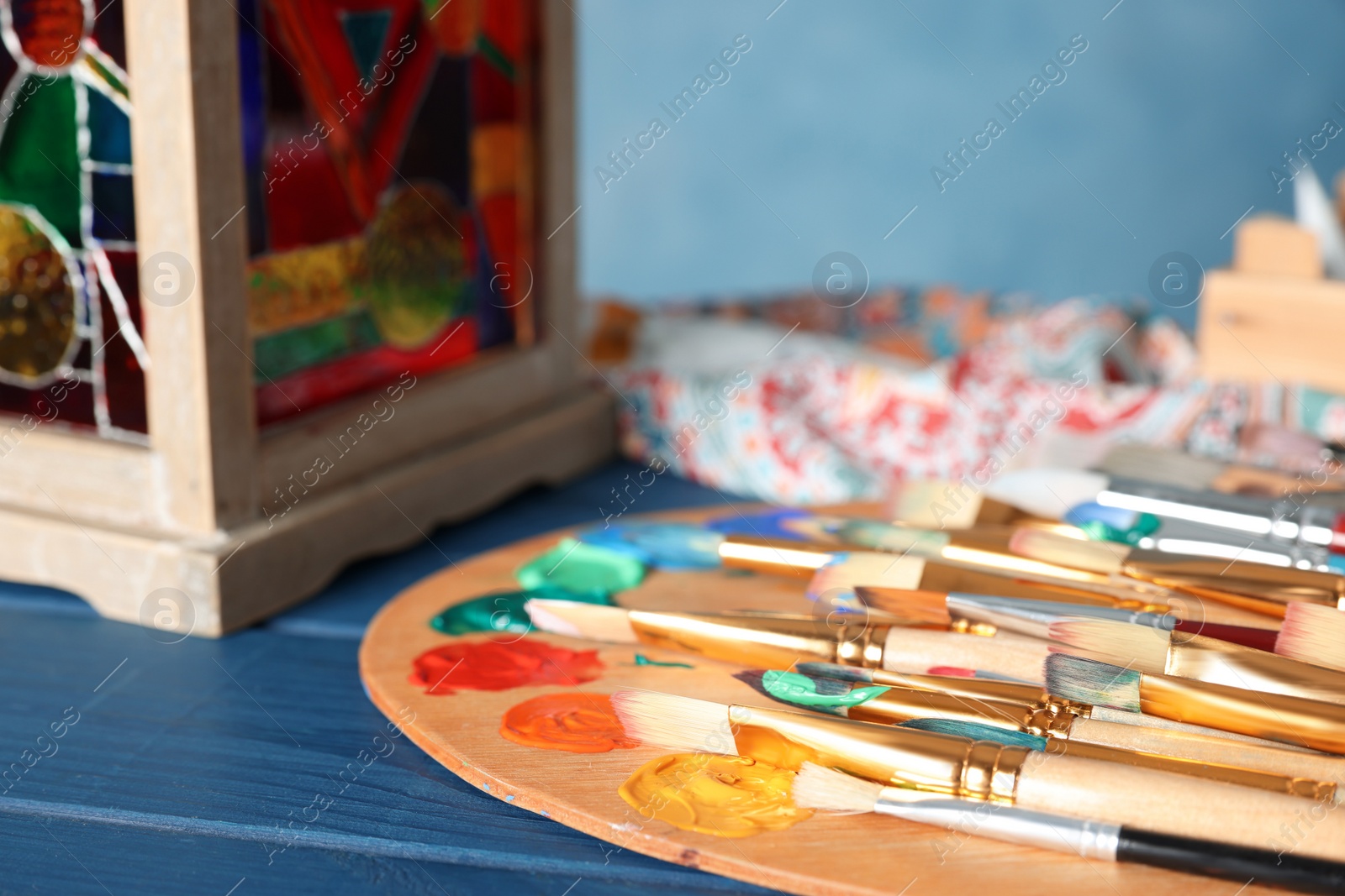 Photo of Many paintbrushes and palette on blue wooden table, closeup