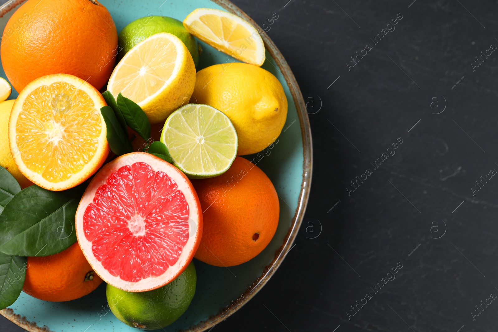 Photo of Different cut and whole citrus fruits on black table, top view. Space for text