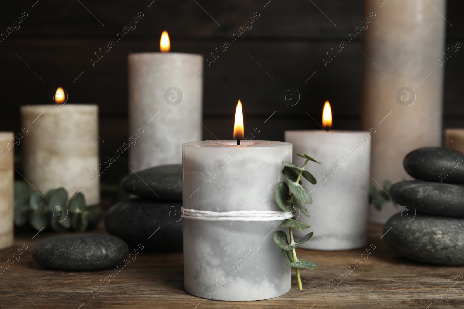 Photo of Composition with burning candles, spa stones and eucalyptus on wooden table