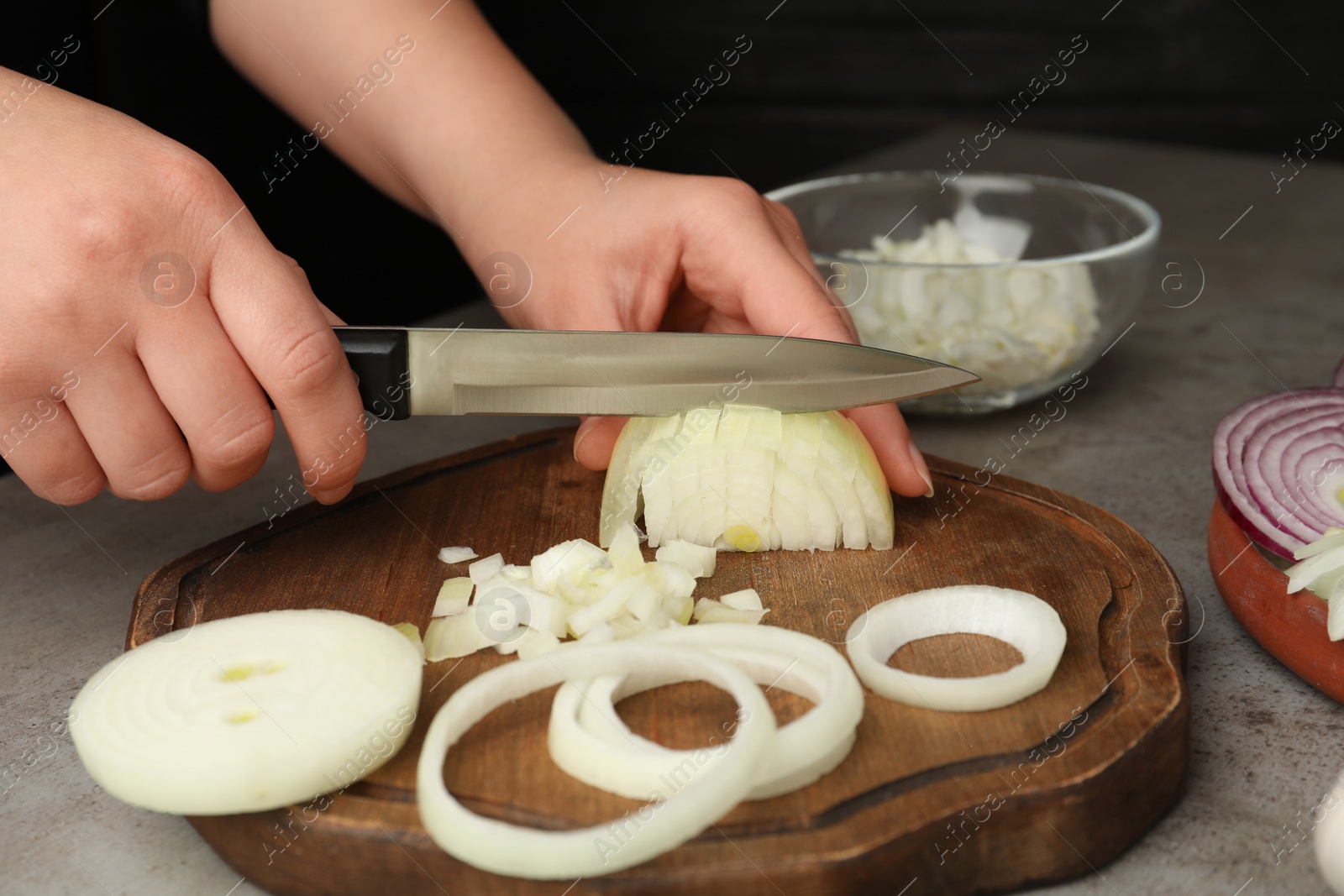Photo of Woman cutting fresh onion on wooden board, closeup