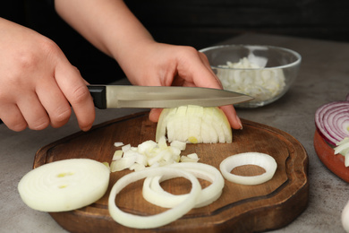 Woman cutting fresh onion on wooden board, closeup