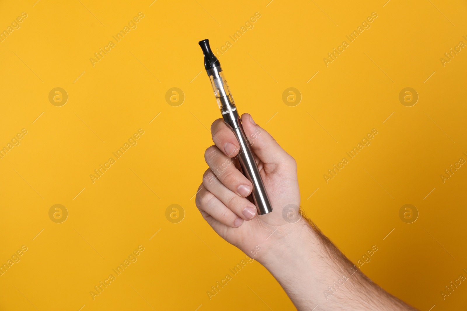 Photo of Man holding electronic cigarette on yellow background, closeup