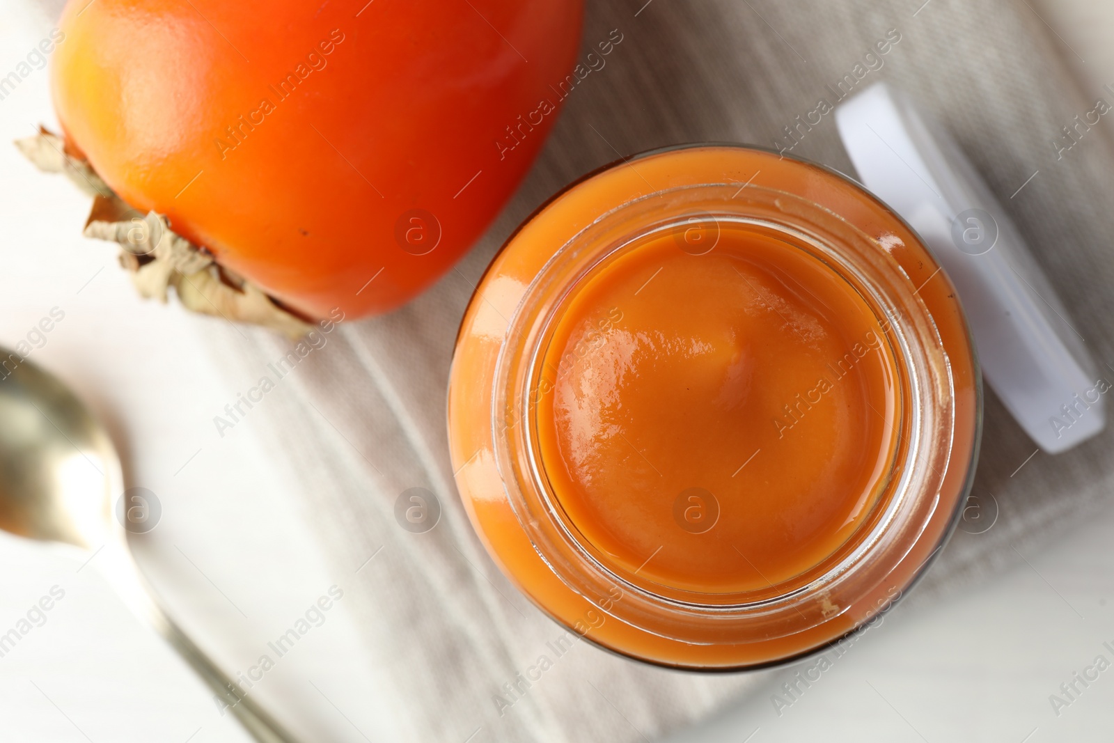 Photo of Delicious persimmon jam in glass jar and fresh fruit on white table, flat lay