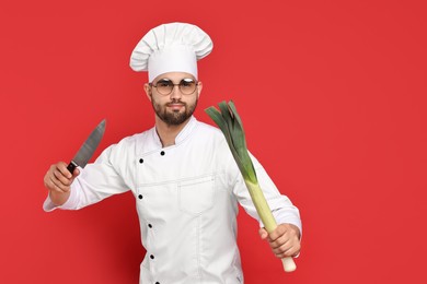 Photo of Professional chef with leek and knife having fun on red background. Space for text