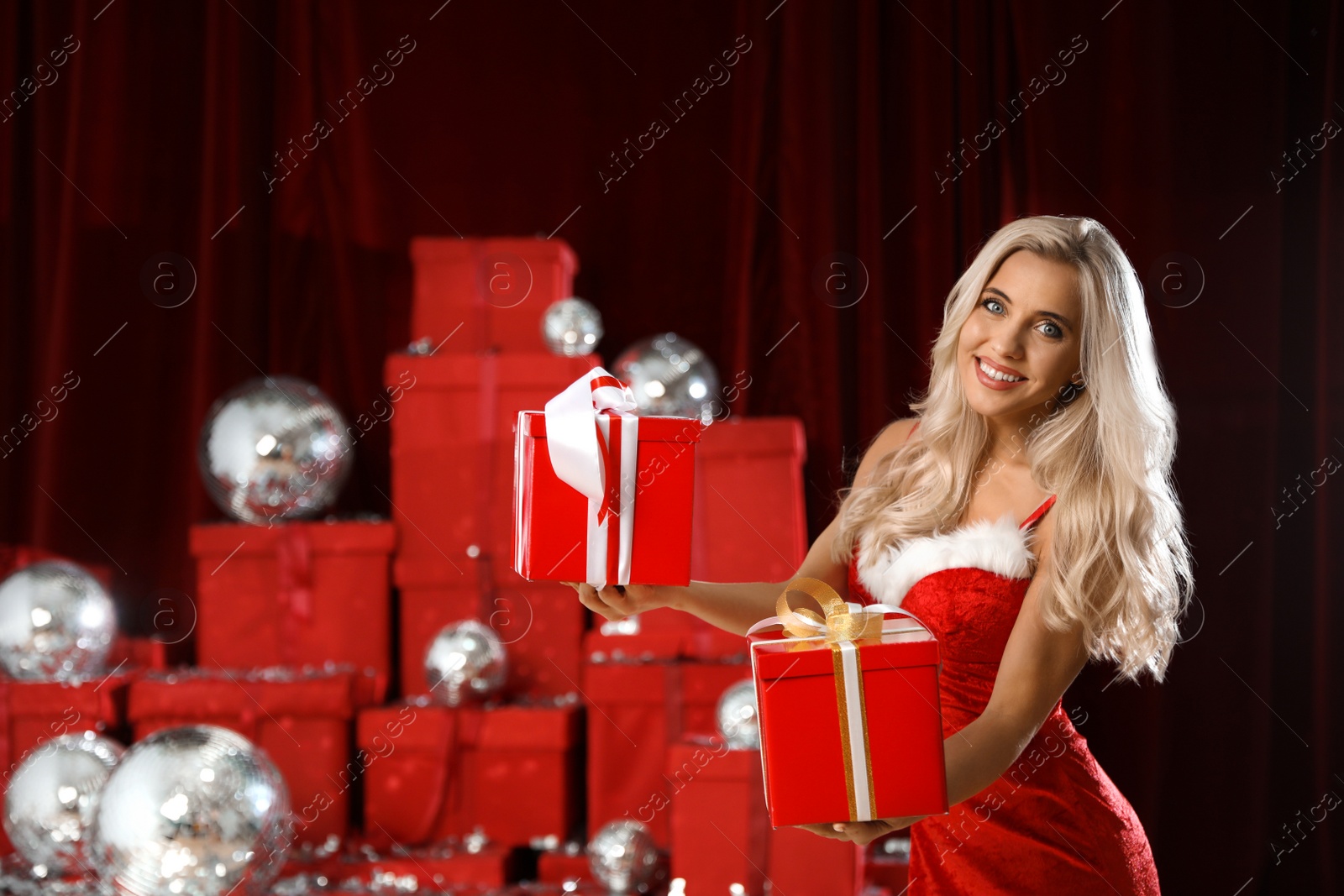 Photo of Beautiful woman with Christmas gifts near pile of presents indoors