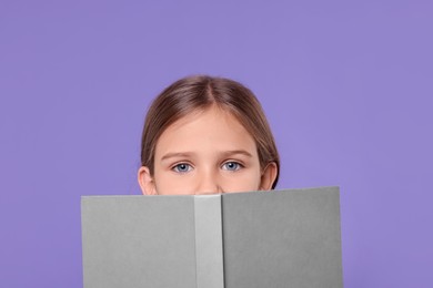 Cute schoolgirl with open book on violet background
