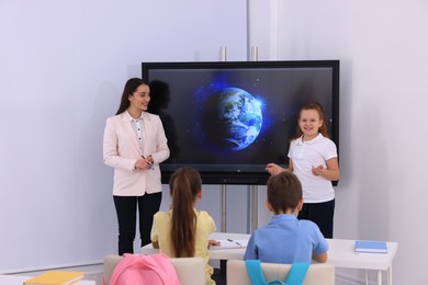 Photo of Teacher and pupil near interactive board in classroom during lesson