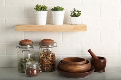 Photo of Wooden dishware and different products on grey table near white brick wall in kitchen