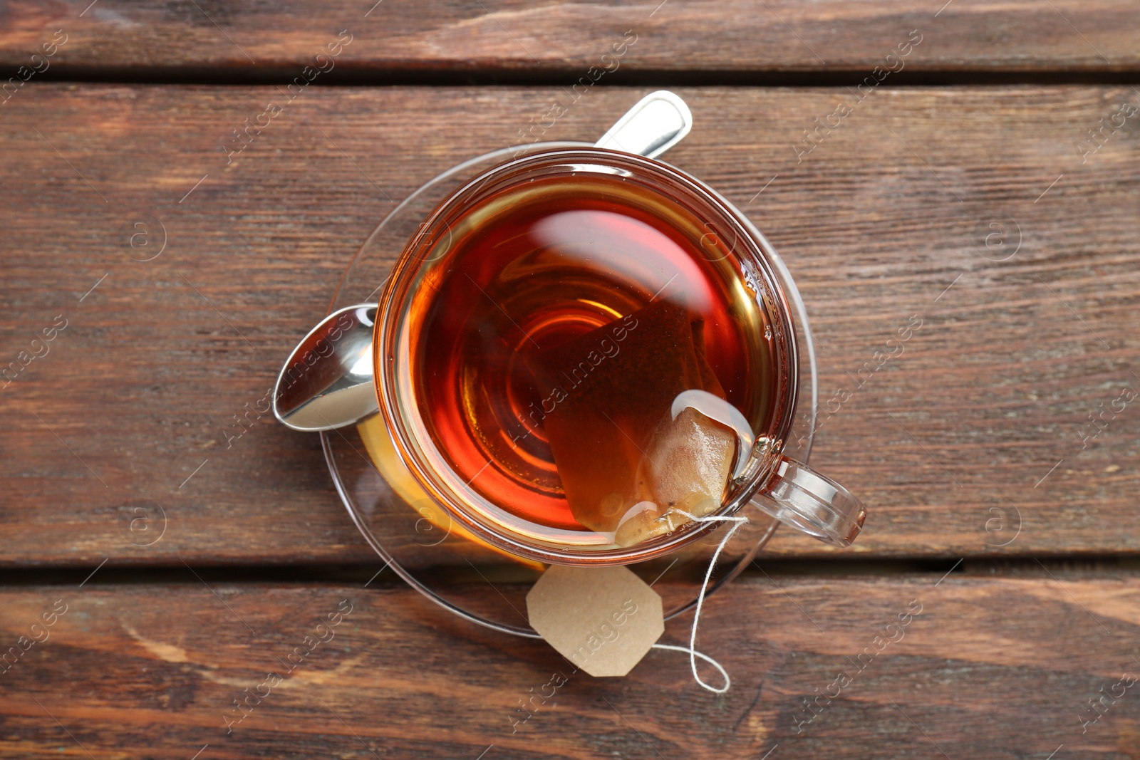 Photo of Brewing aromatic tea. Cup with teabag and spoon on wooden table, top view