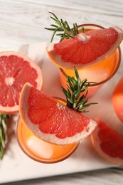 Photo of Tasty grapefruit drink with ice in glasses, rosemary and fresh fruits on light wooden table, top view