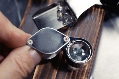 Professional jeweler working with gemstone at wooden table, closeup