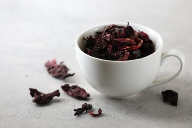 Aromatic hibiscus tea. Dried roselle calyces in cup on light table, closeup and space for text