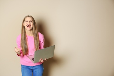 Photo of Emotional young woman with laptop celebrating victory on color background. Space for text