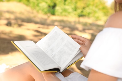 Photo of Young woman reading book outdoors, closeup view