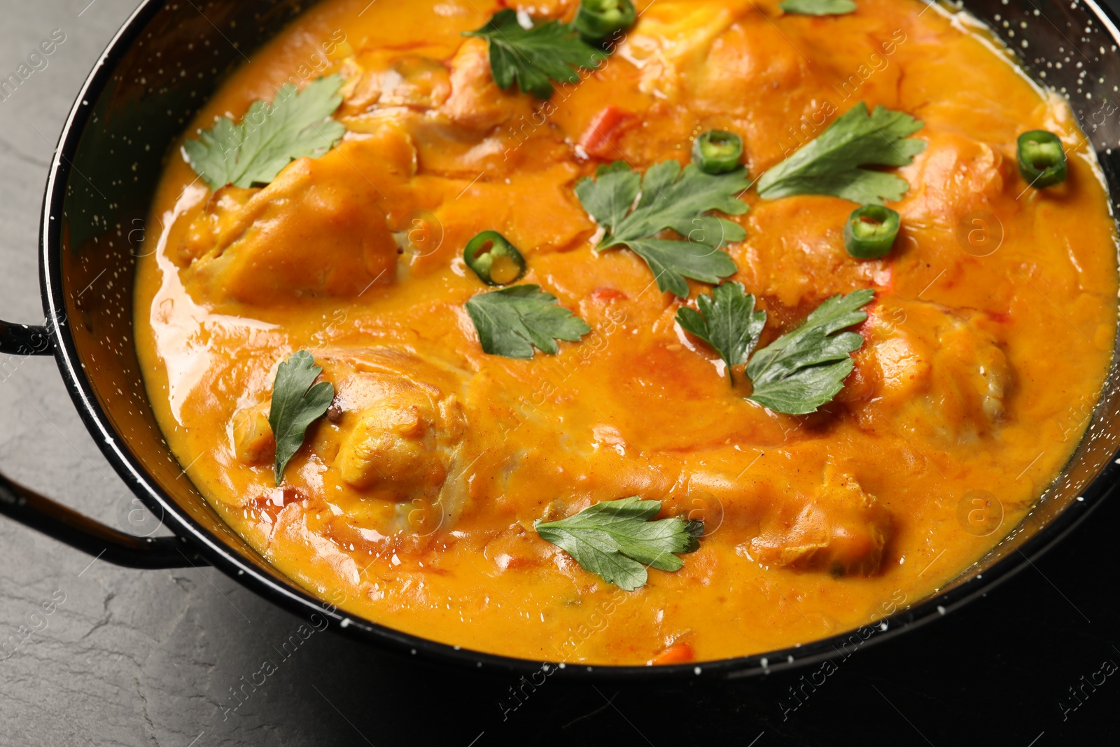 Photo of Tasty chicken curry with parsley and pepper on black textured table, closeup