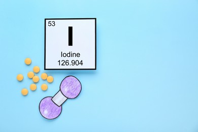 Card with iodine element, atom made of paper and pills on light blue background, flat lay. Space for text