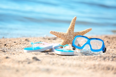Starfish, goggles and flip flops on sand near sea. Beach object