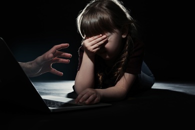 Stranger reaching frightened little child with laptop on dark background. Cyber danger