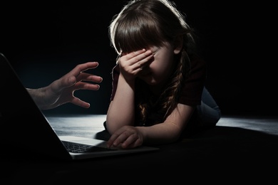 Photo of Stranger reaching frightened little child with laptop on dark background. Cyber danger