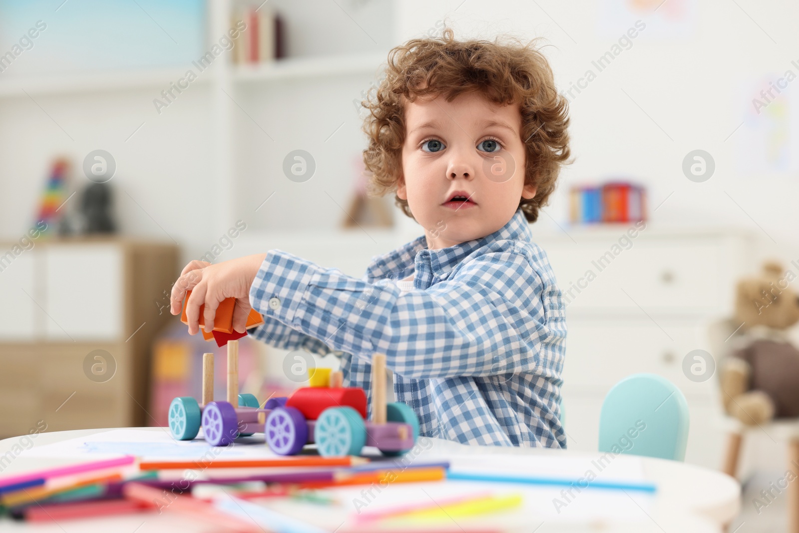 Photo of Cute little boy playing with wooden toys at white table in kindergarten