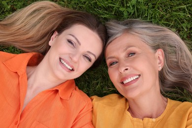 Photo of Happy mature mother and her daughter lying on green grass, top view