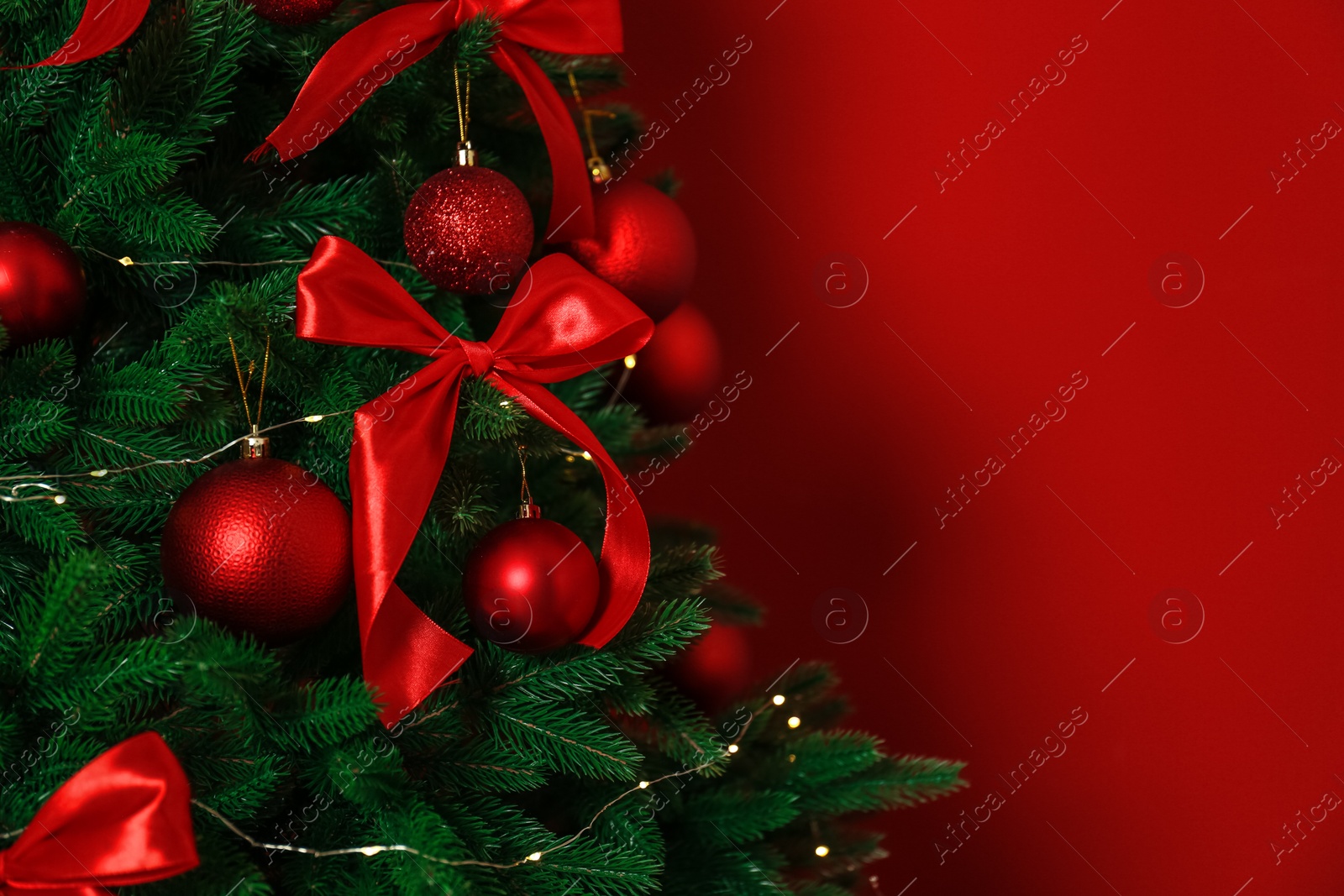 Photo of Decorated Christmas tree on red background, closeup. Space for text