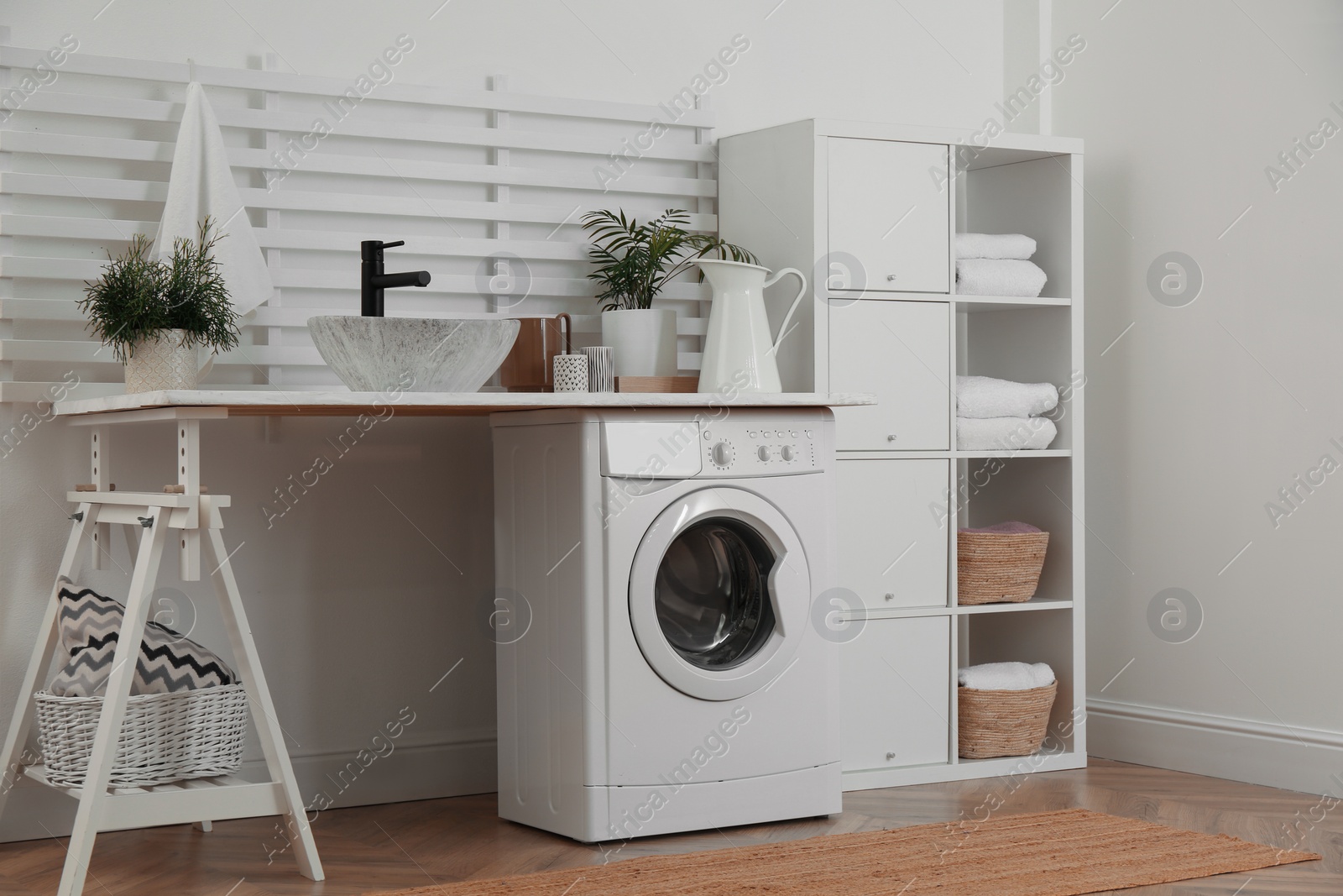 Photo of Laundry room interior with modern washing machine and shelving unit near white wall