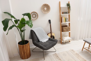 Photo of Spring atmosphere. Stylish room interior with comfortable chair, houseplant and shelving unit