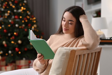 Woman reading book near Christmas tree indoors