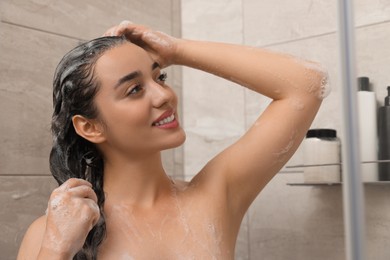Photo of Beautiful happy woman washing hair with shampoo in shower