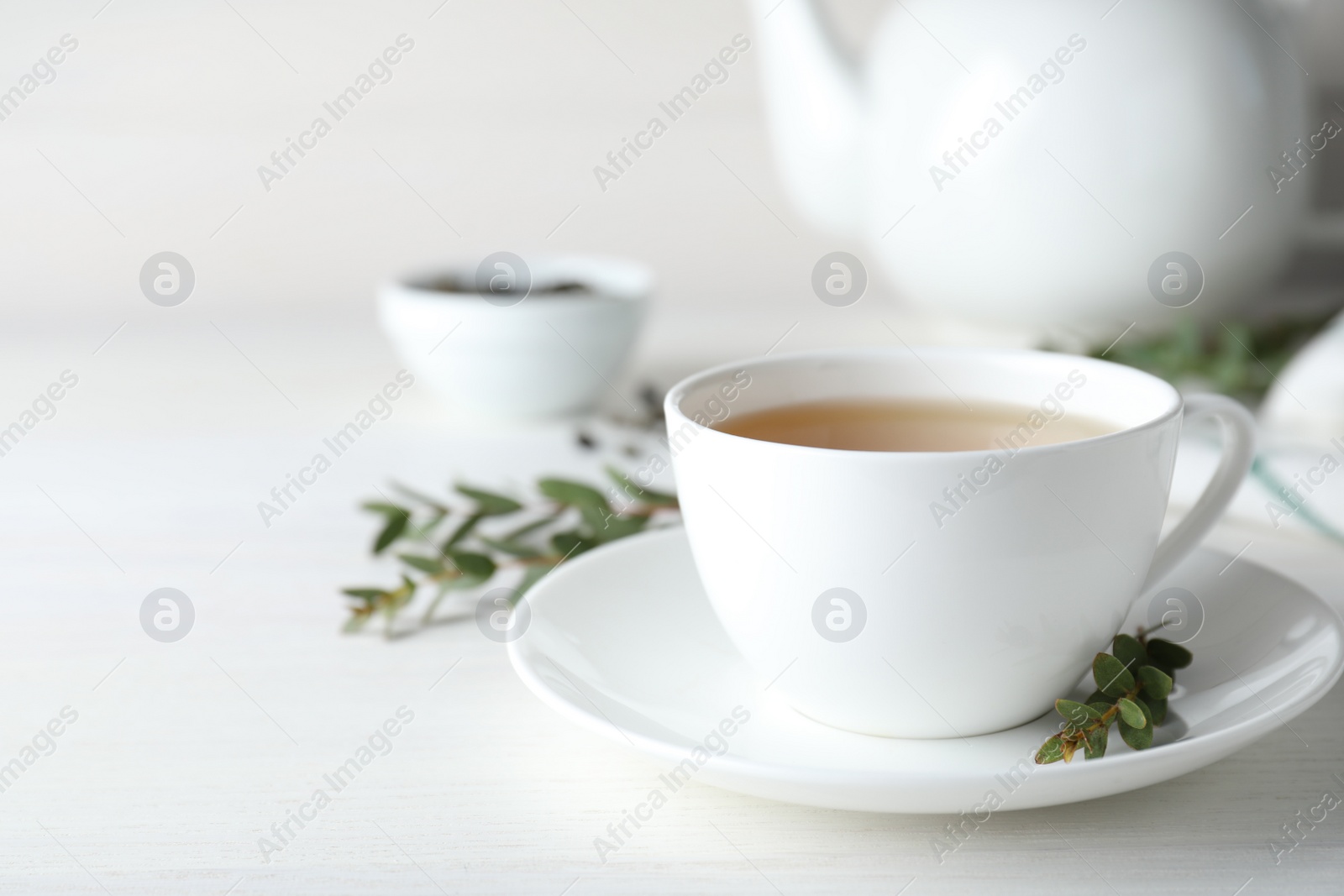 Photo of Cup of green tea and eucalyptus leaves on white table. Space for text