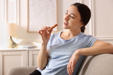 Woman holding tasty granola bar at home