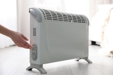 Woman turning on electric heater at home, closeup