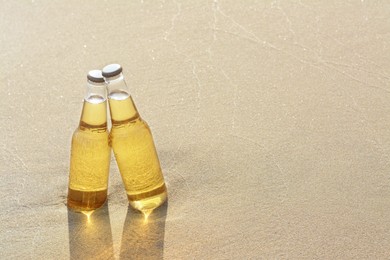 Photo of Bottles of cold beer on sandy beach. Space for text