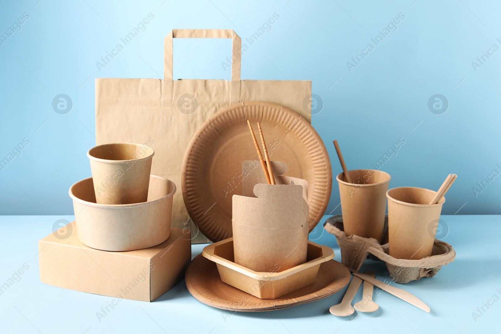 Photo of Eco friendly food packaging. Paper containers, tableware and bag on white table against light blue background