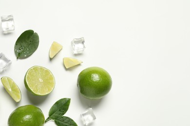 Photo of Fresh ripe limes with green leaves and ice cubes on white background, flat lay