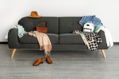 Photo of Messy pile of clothes on sofa and shoes in living room